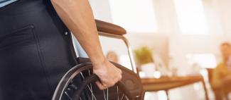 Main d'une personne à mobilité réduite sur la roue d'un fauteuil roulant
